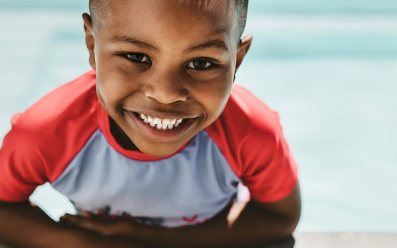 lifestyle image of a boy smiling on a pool's edge